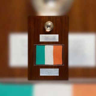 a wooden plaque displays a stone inside a lucite sphere and a green, white and orange striped flag.