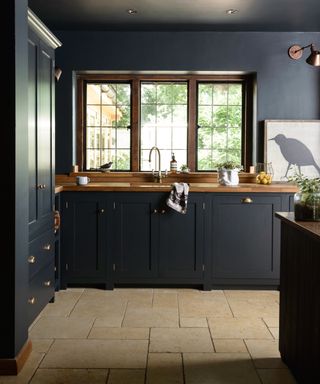 inky blue kitchen with painted cabinets and matching walls and ceiling, wooden countertops and windows, traditional stone flags