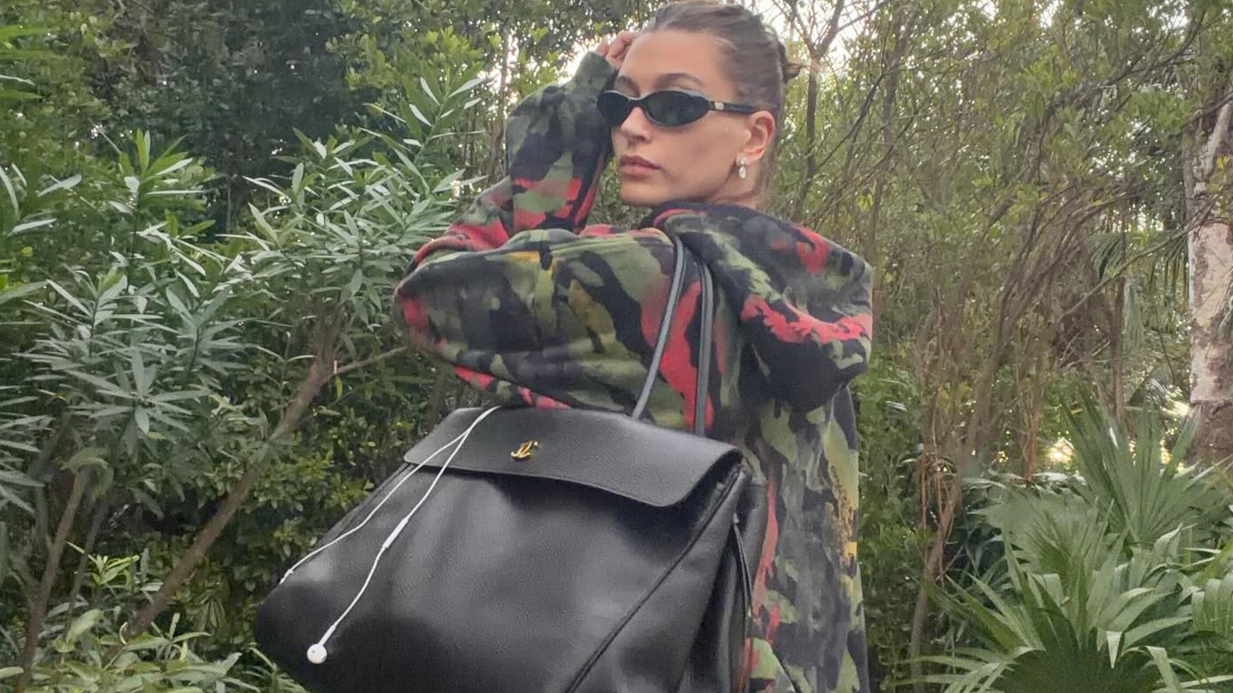 Hailey Bieber wears a camouflage sweatshirt and black bag with camouflage pants.