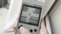A hand taps the emulated d-pad of an original Game Boy on an ereader device. Pokemon Blue is being played in greyscale.