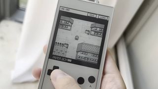 A hand taps the emulated d-pad of an original Game Boy on an ereader device. Pokemon Blue is being played in greyscale.