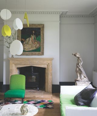 A bright white living room with statement marble fireplace and statue, with green accents and yellow and white pendant light