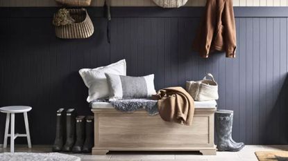 A dark blue entryway with a storage ottoman and hanging coats