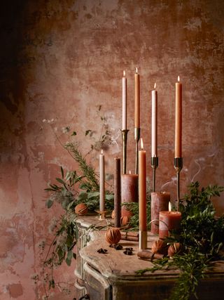 Selection of lit red candles in metal candlesticks on a wooden sideboard.