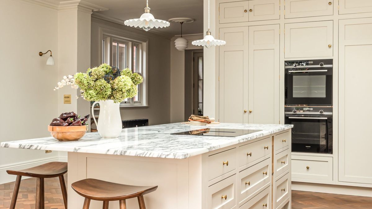 A kitchen island with a marble worktop, built in hob and seating in a shaker kitchen