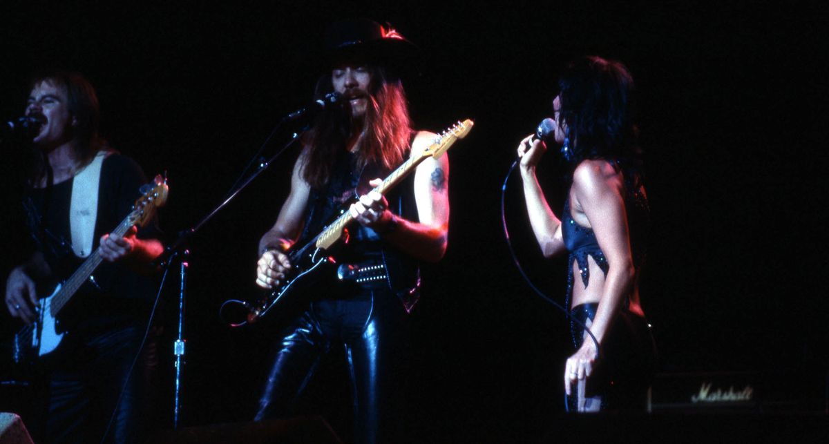 Les Dudek takes a solo on a black Strat as Cher stands to his right.