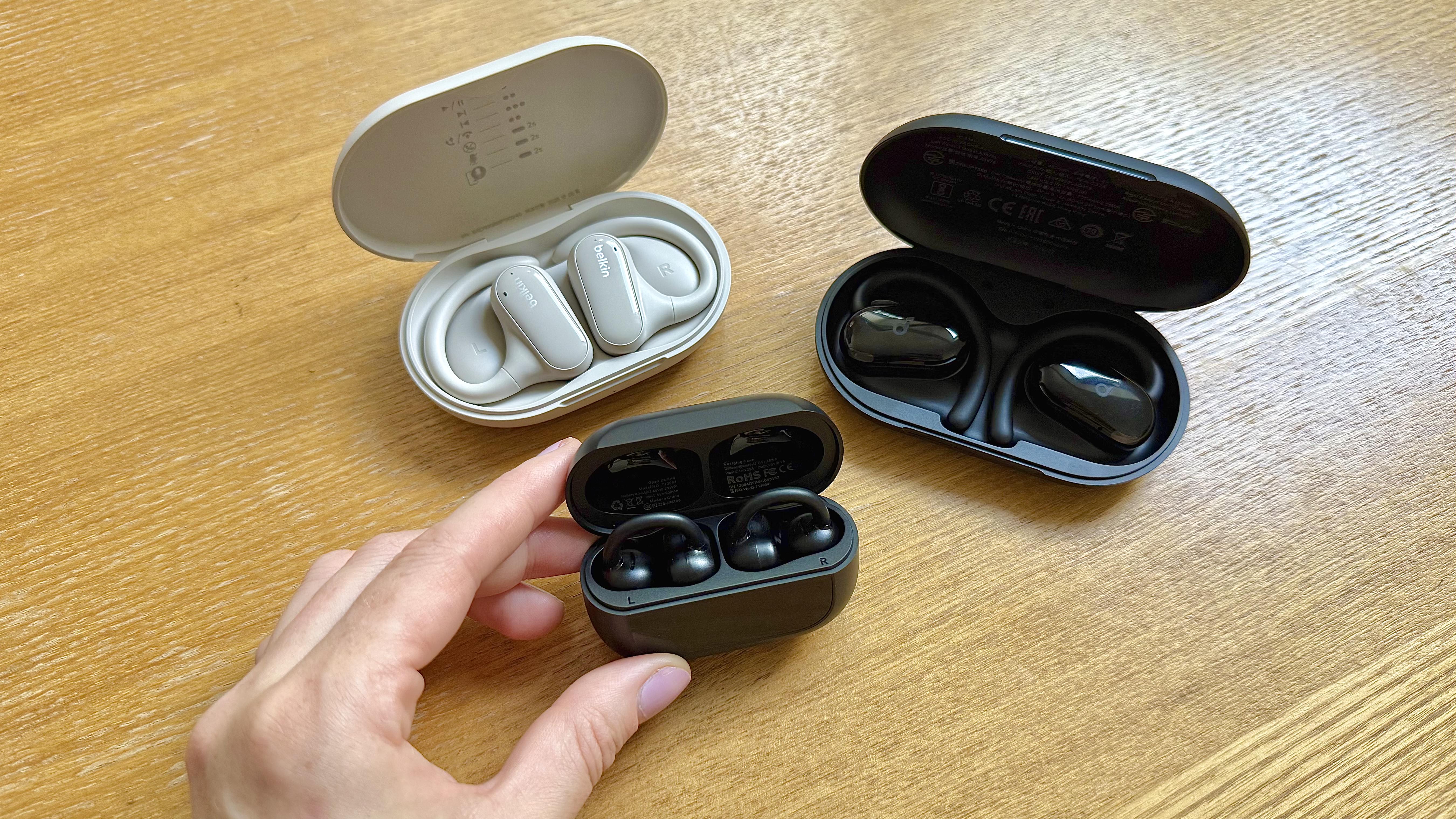 Three pairs of open earbuds pictured in their charging case on a wooden surface