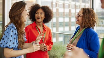 Three women smile and laugh while connecting at a networking event.