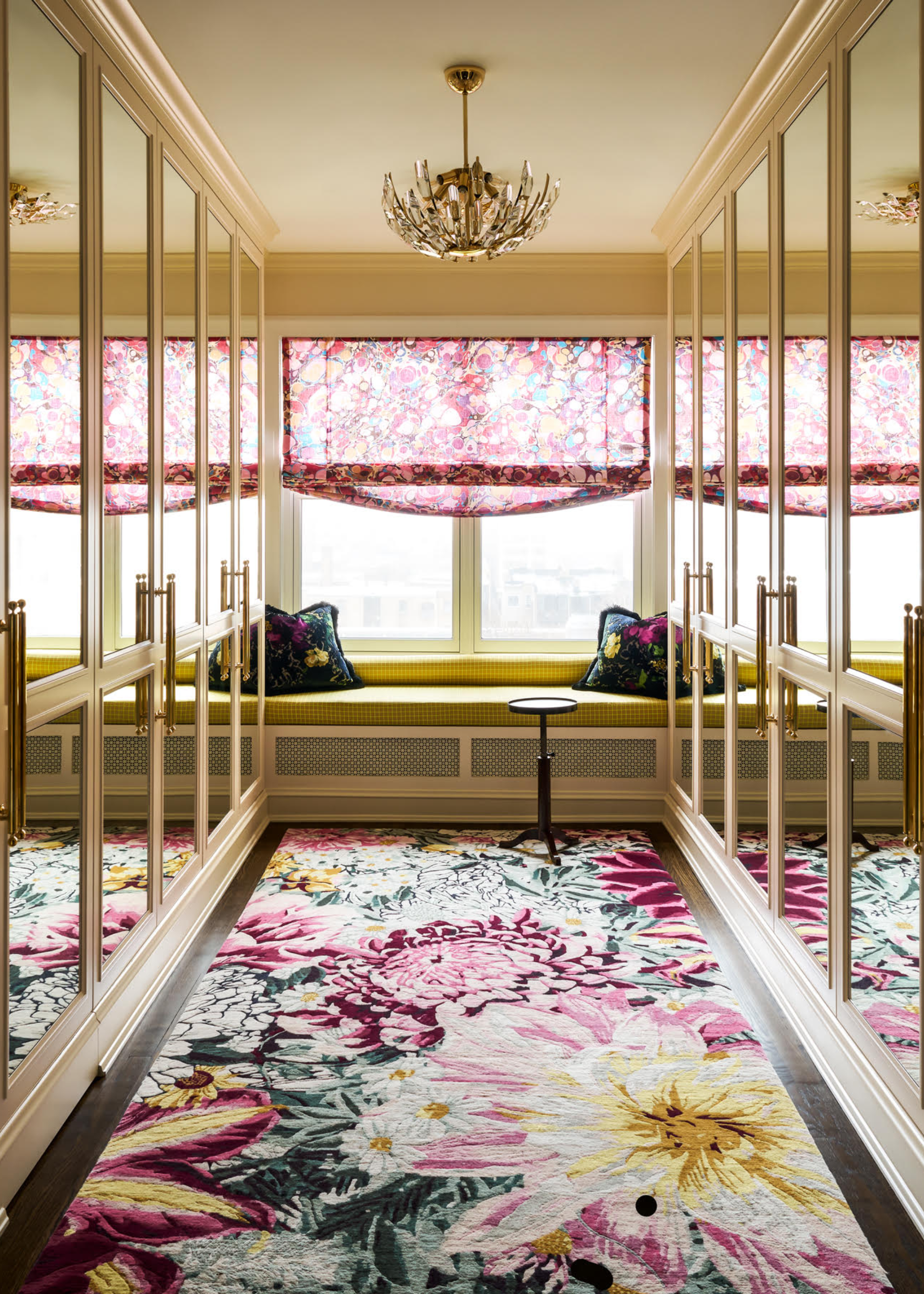 A luxe walk-in wardrobe with mirrored doors, in-built seating, and a floral rug