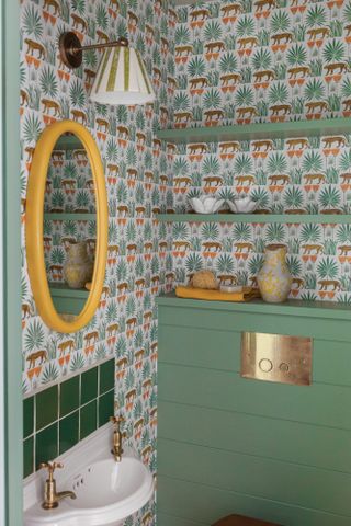 Bathroom with green cabinetry, green and rust wallpaper and yellow mirror