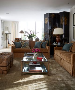 Two brown sofas with blue cushions in front of a dining area and a black and gold screen
