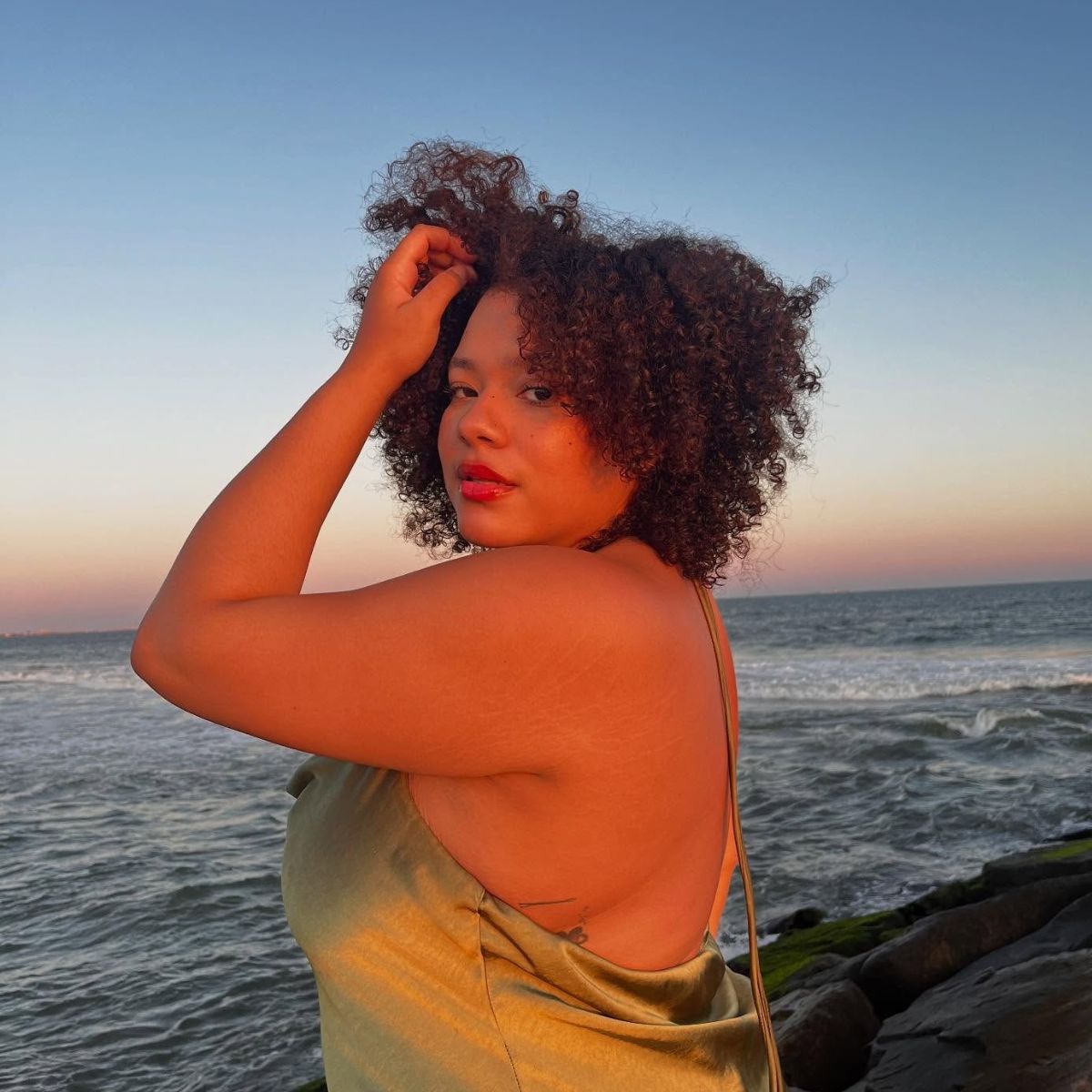 A woman standing in front of the sea at sunset