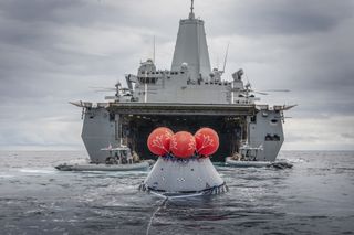 NASA's Orion crew capsule floats behind the USS John P. Murtha in the Pacific Ocean after the landing and recovery crews from the Exploration Ground Systems team at the agency's Kennedy Space Center performed their first full mission profile test of recovery procedures for the Artemis 1 mission, on March 13, 2020. Scheduled to launch in the second half of 2021, the Artemis 1 mission will mark the first uncrewed test flight of NASA's Space Launch System megarocket and Orion spacecraft.