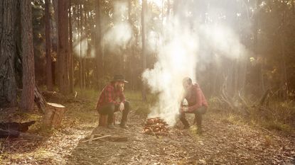Men in bushland sitting around campfire