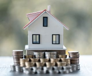 cardboard model of house sat on different piles of coins