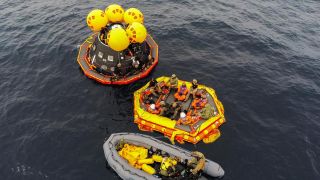 an overhead view of a spacecraft in the water, alongside two rafts.