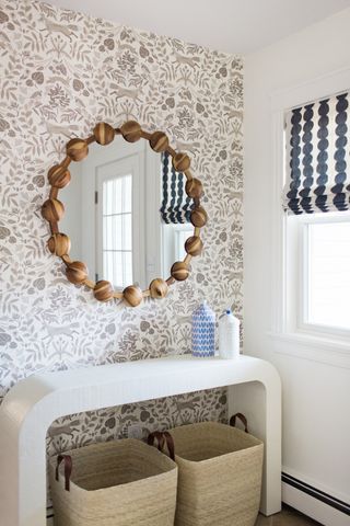 Light fall colored woodland wallpaper print in utility space with decorative round mirror, woven laundry baskets and fabric blinds