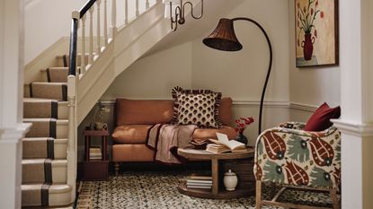 A cozy seating area with a small sofa and an arm chair nestled under a curling stair case. A large sculptural lamp beside them and a low hanging pendant.