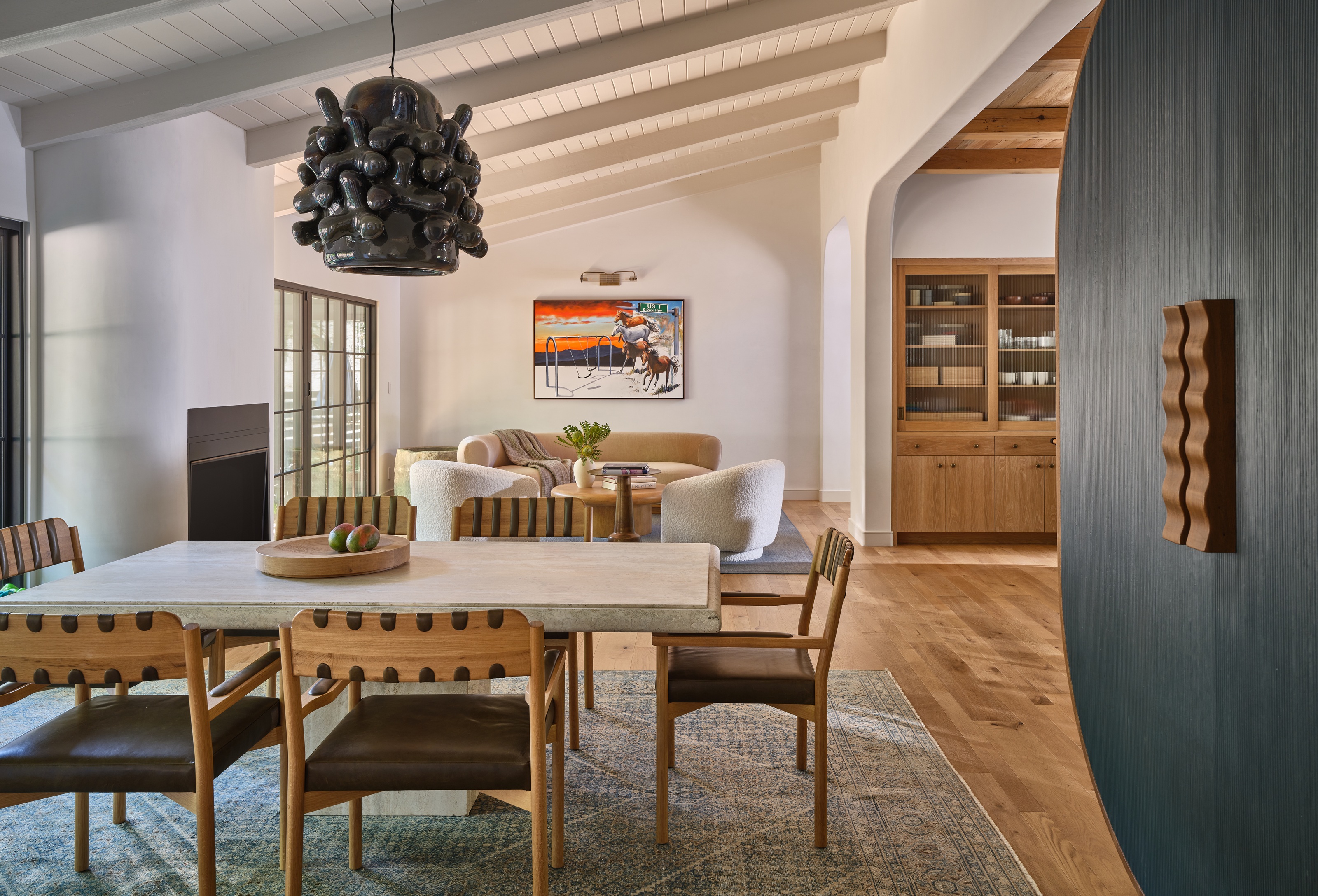 a mid century house with a dining table and intriguing ceiling light, a view through to a living room and part of a kitchen