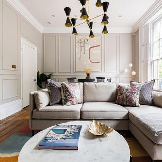 Oval coffee table with gold leaf ornament next to grey L-shaped couch with black and gold light hanging from the ceiling