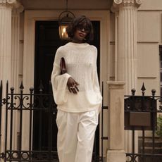 A woman wearing a white sheer knit with white trousers and matching kitten-heel pumps. 