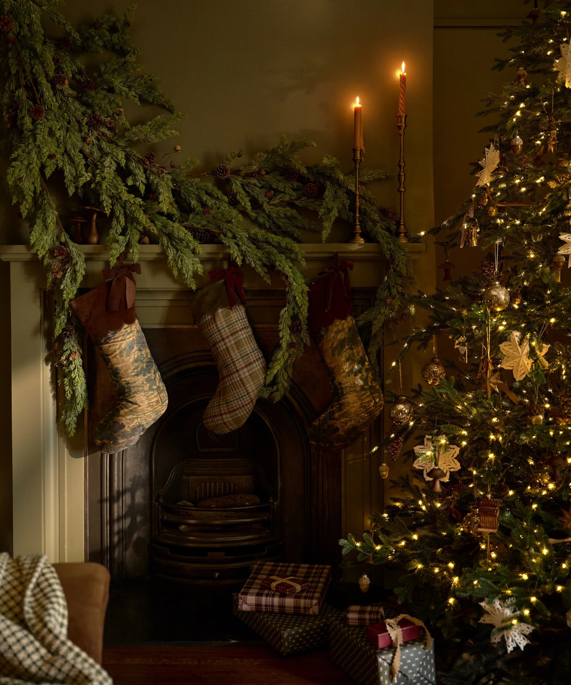 a cozy living room with a large fireplace and stockings hung from the mantel, a large garland strand, and a christmas tree decorated with lights and ornaments