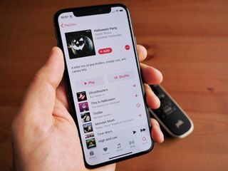 Hand holding a Space Gray iPhone X with a Halloween Playlist open on Apple Music