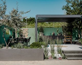 An outdoor kitchen within a garden setting with walls painted in sage green