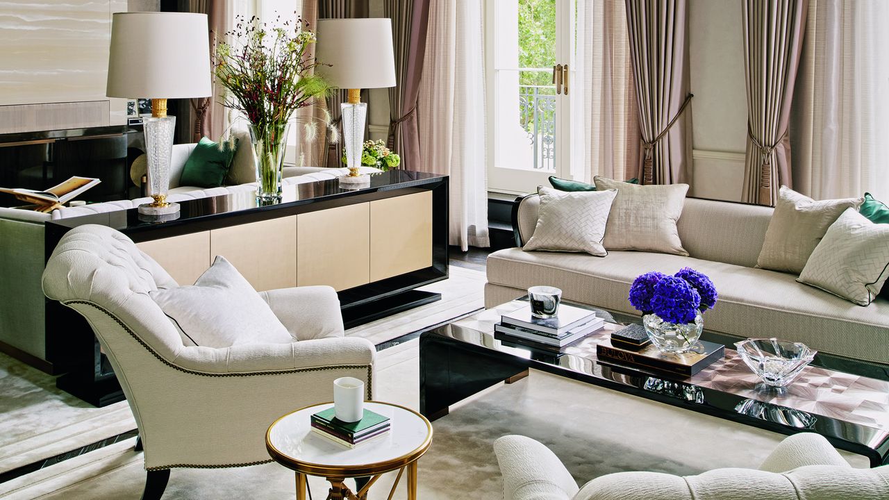 white living room with cream sofa and armchairs, cream rug, black coffee table and brass chandelier