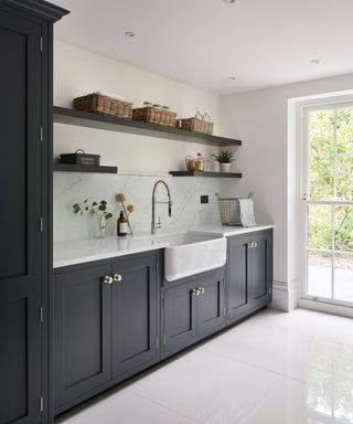 A modern Davonport laundry room with dark blue cabinetry, sleek white floors, floating shelves, and a door to the right