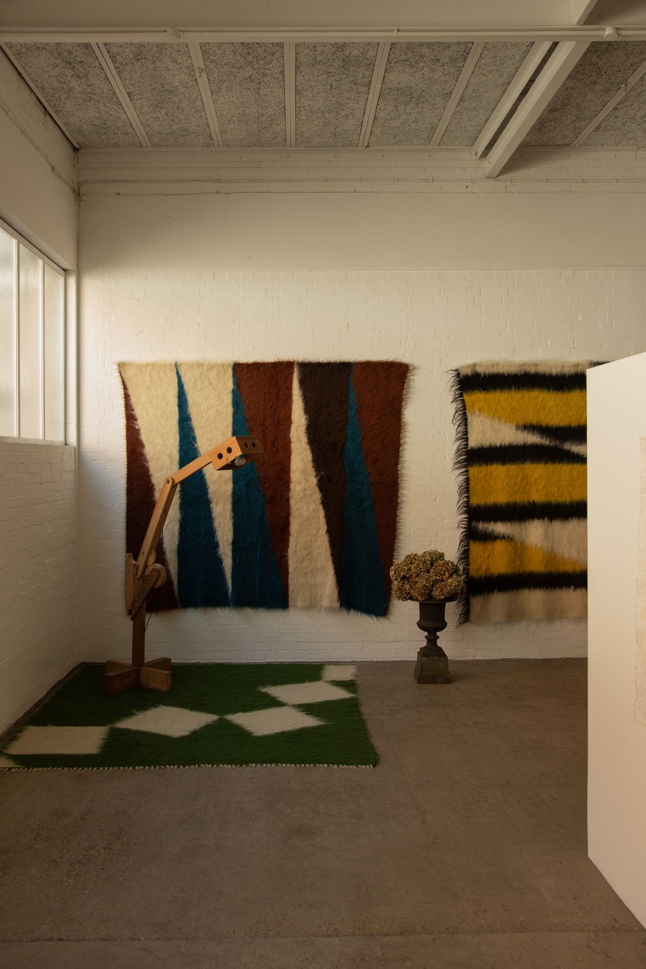 A series of textile creations with an abstract, textural wool feel sit in an industrial showroom alongside iconic modernist designs.