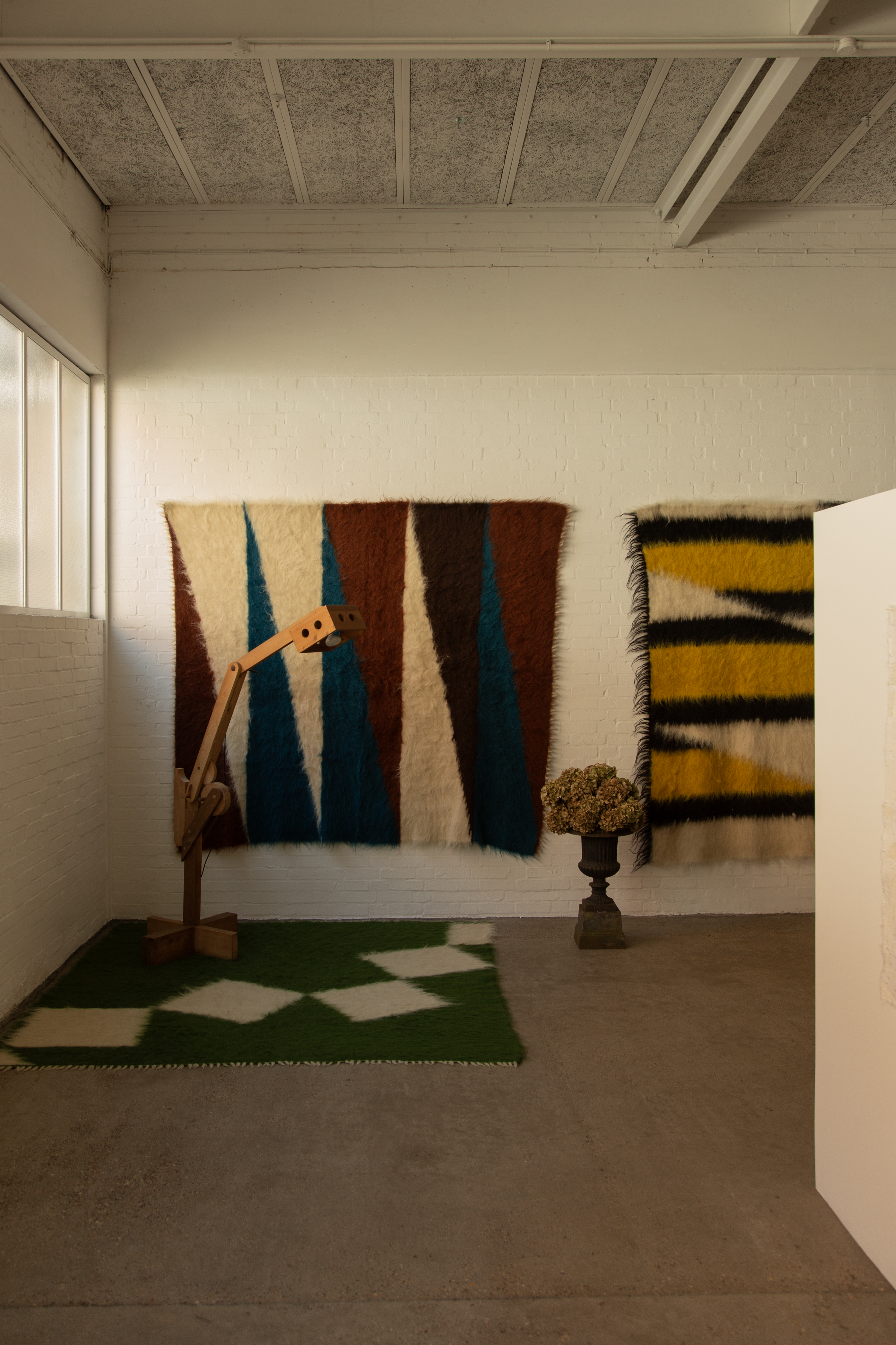A series of textile creations with an abstract, textural wool feel sit in an industrial showroom alongside iconic modernist designs.