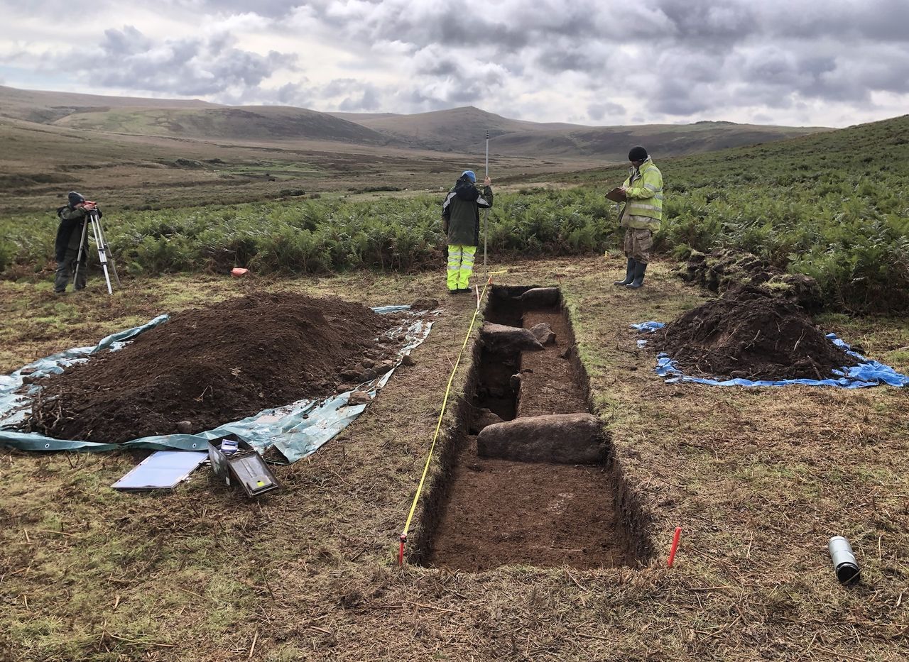 Three people dig out a rectangular excavation site