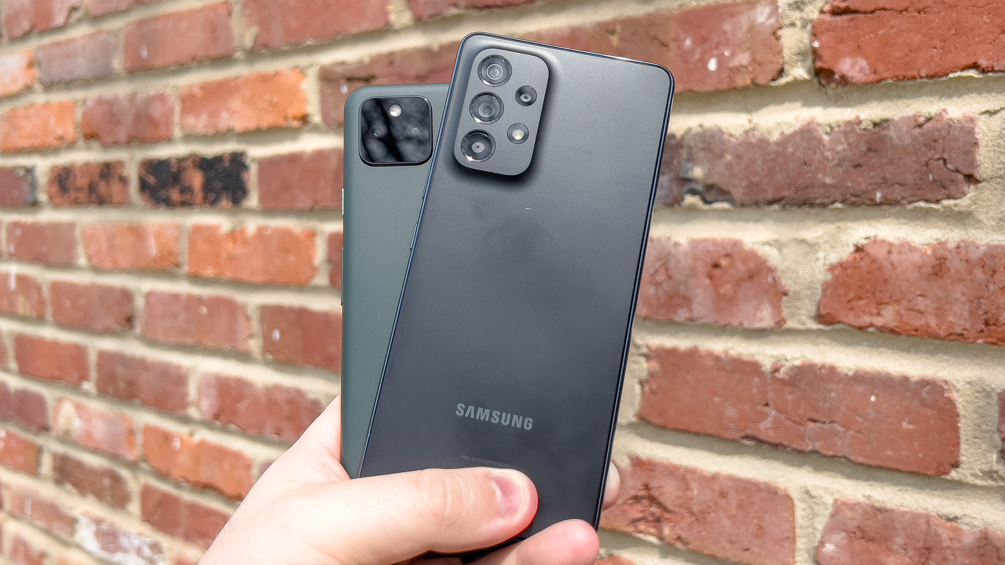 galaxy a53 and pixel 5a in hand against brick background