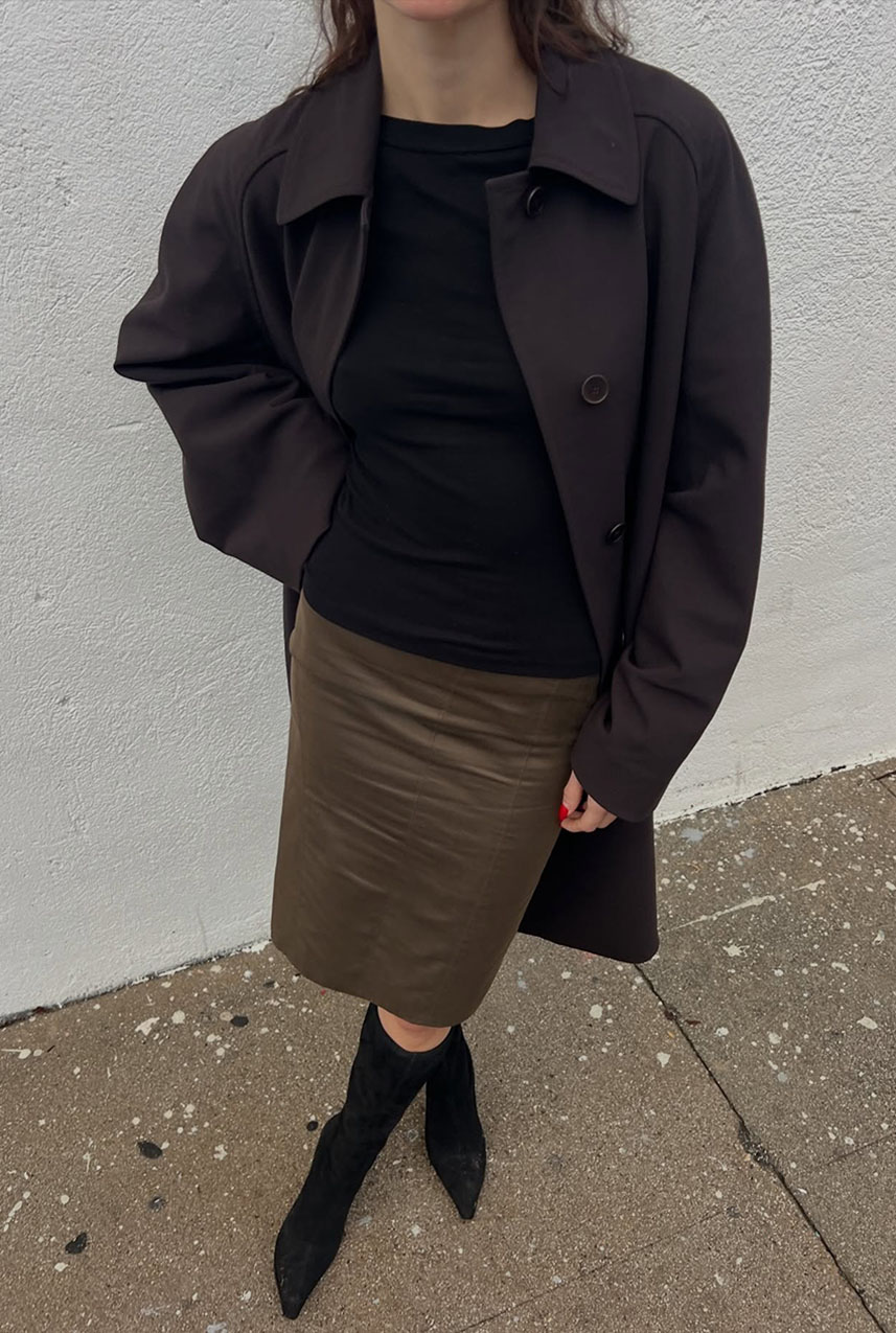 a woman wearing a brown coat over a black shirt, a brown skirt, and black boots