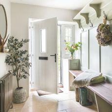 Autumnal hallway with sage green wall panelling and an autumnal wreath, and the white front door open next to an olive tree