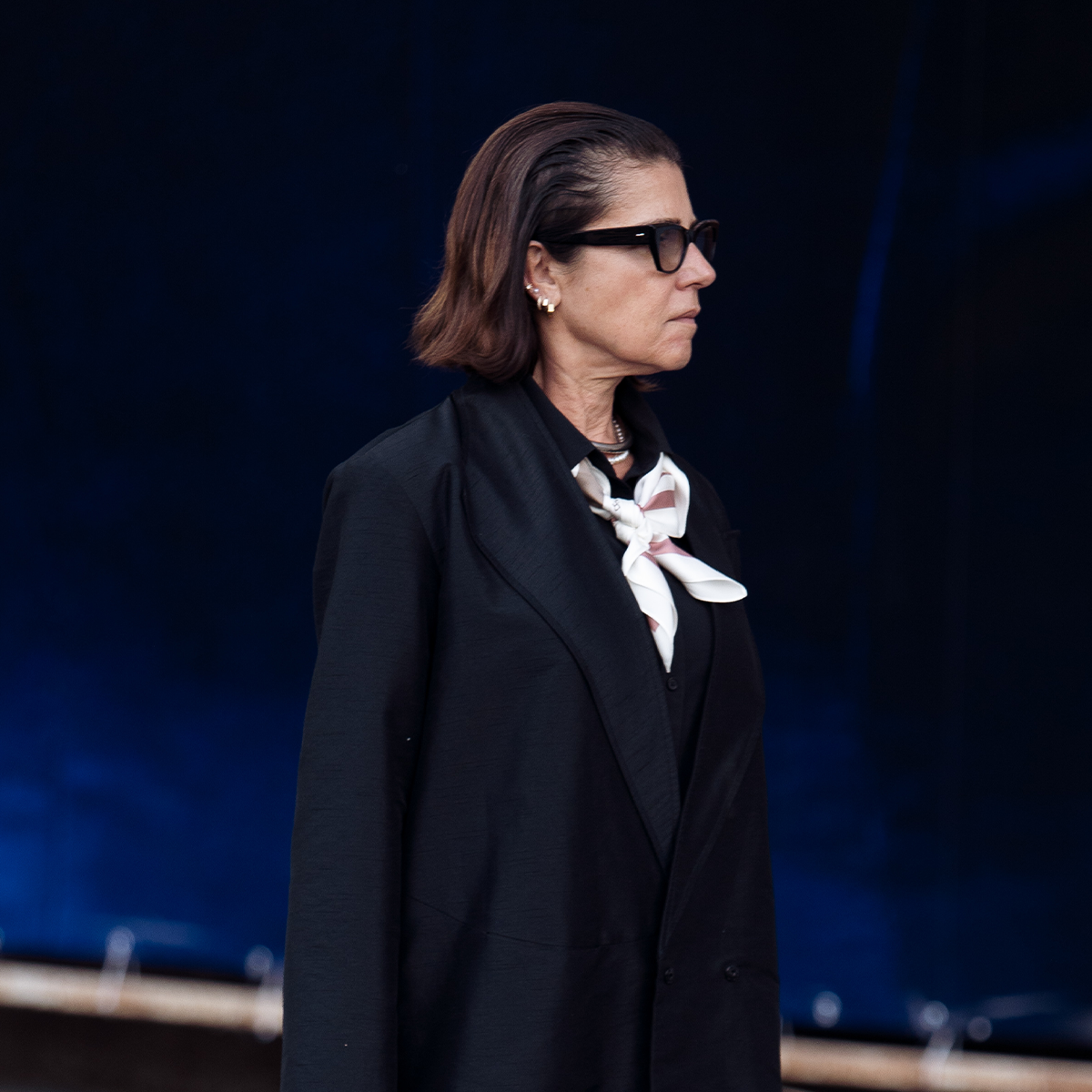 Woman wearing black jacket, black platform sneakers, and black trousers in street style photo.