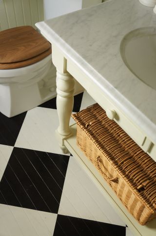 Checkerboard floor with wicker basket under cream bathroom vanity