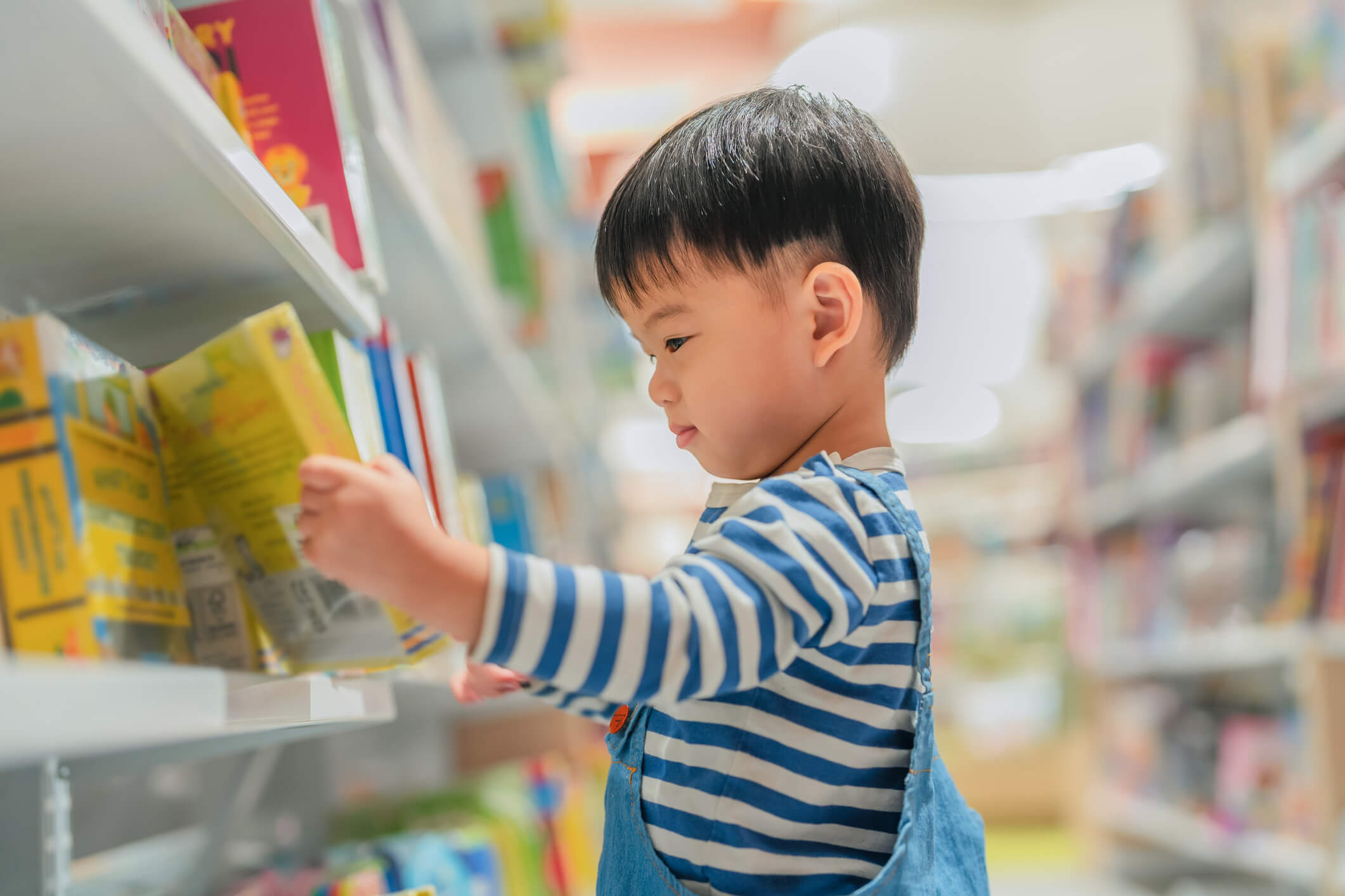 A happy child looking at a book on a shelf