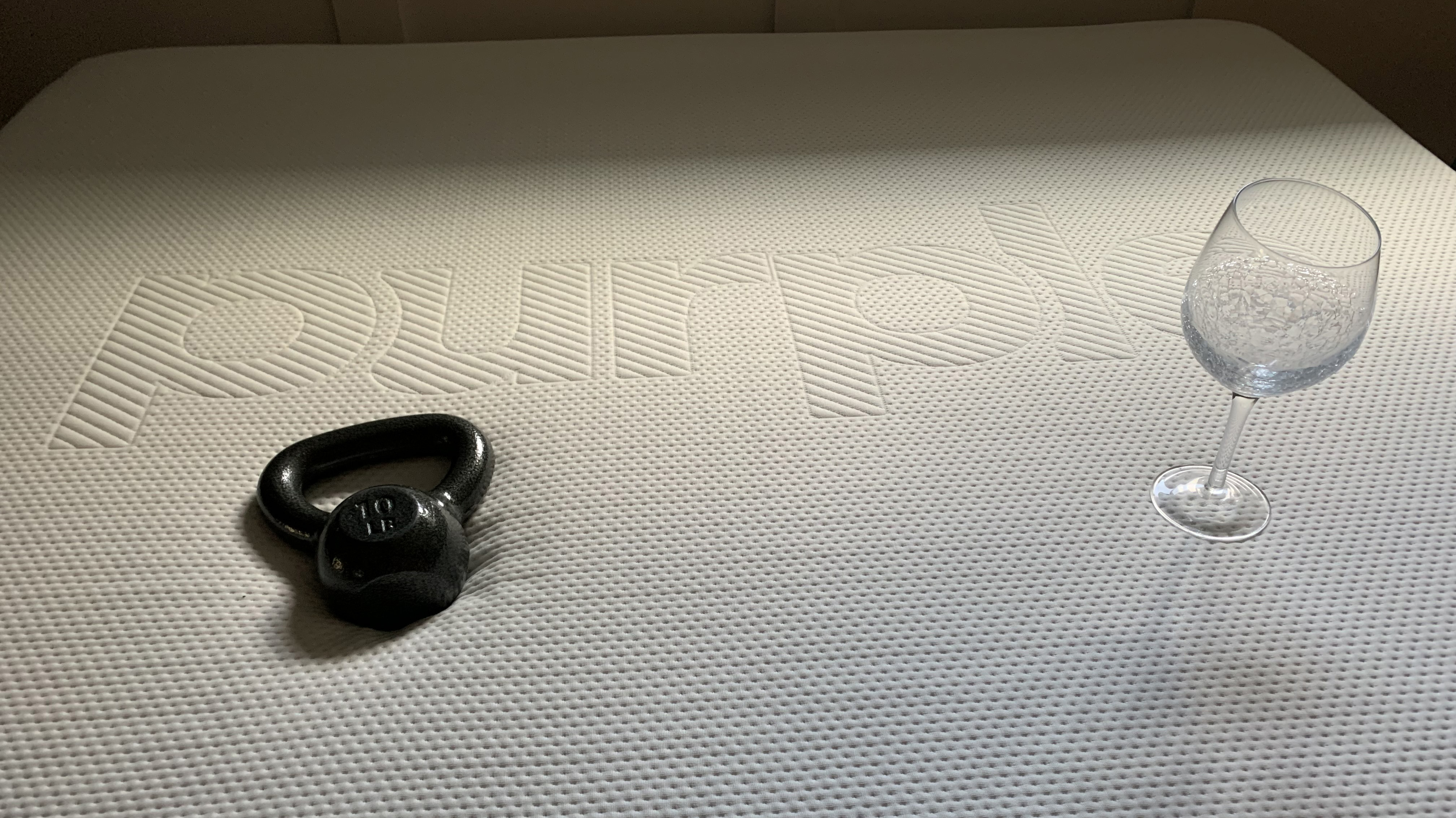 A black kettlebell and a wine glass placed close together on top of the Purple Plus mattress during the review testing process