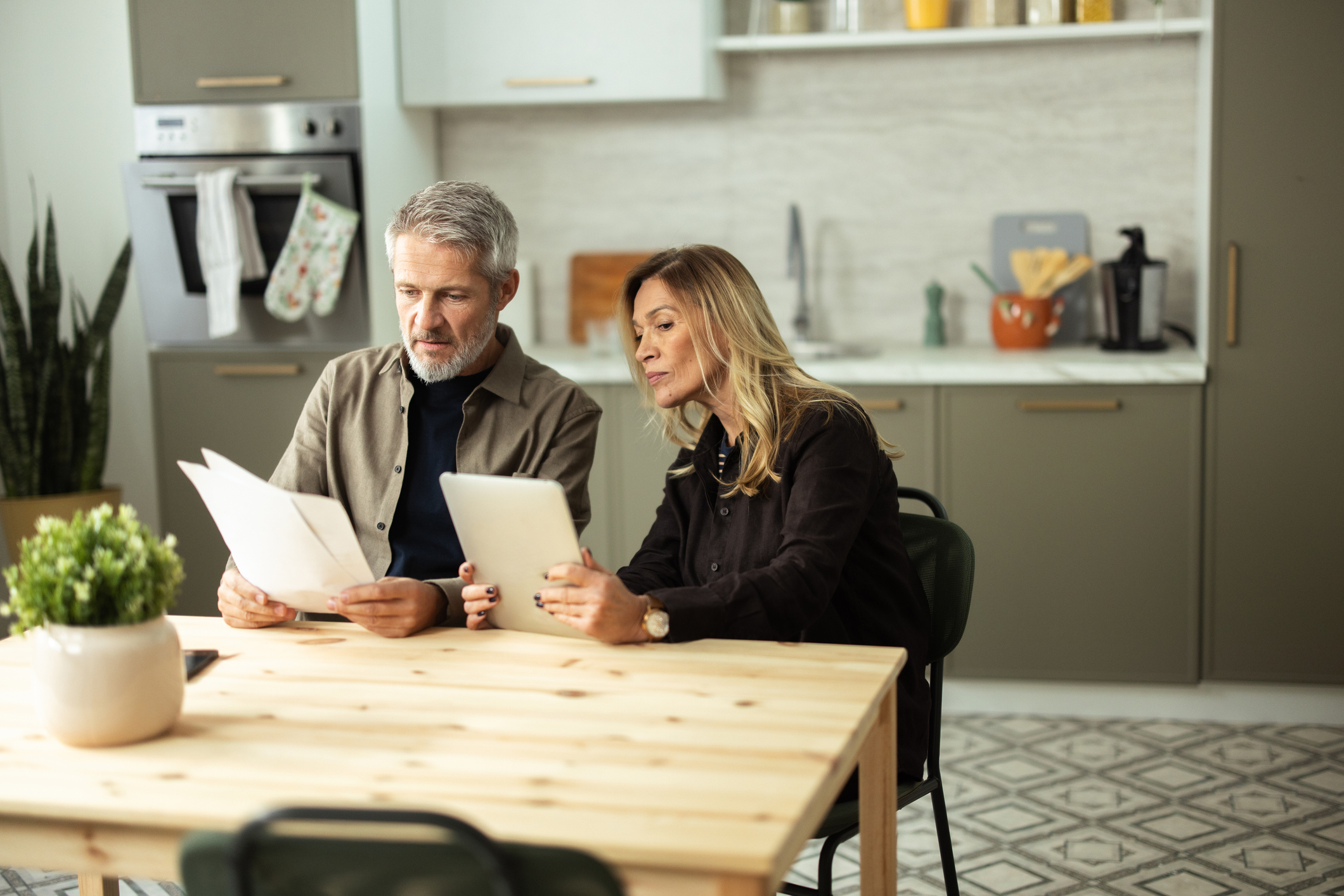 Mature couple reviewing bills and financial documents in their kitchen