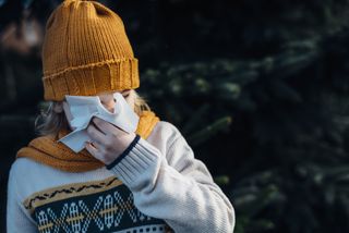 Child blowing nose with yellow hat on in the winter