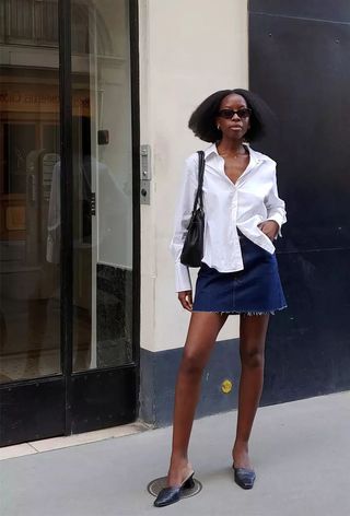 a photo of a woman's classic outfit idea with a white shirt and denim skirt and mules