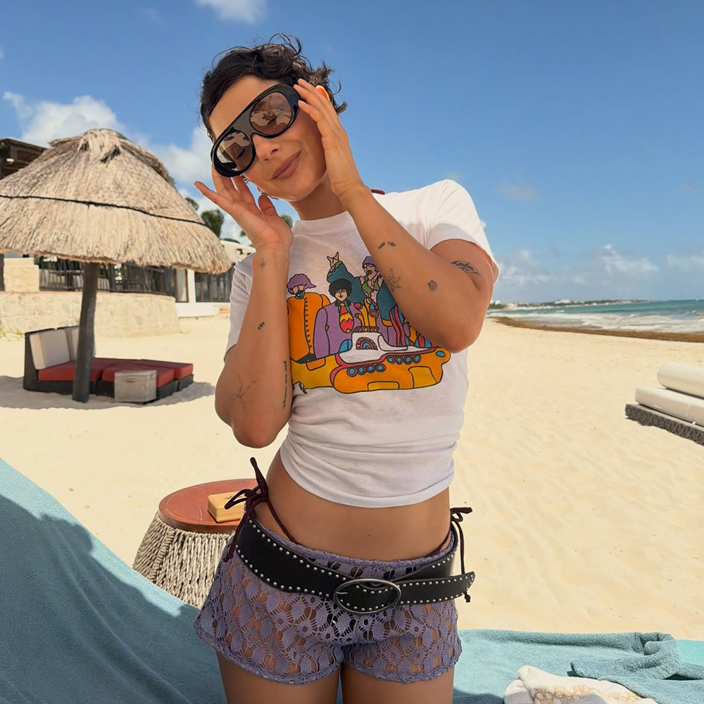 a woman on the beach wearing a white graphic tee, lilac lace short shorts, and large sunglasses