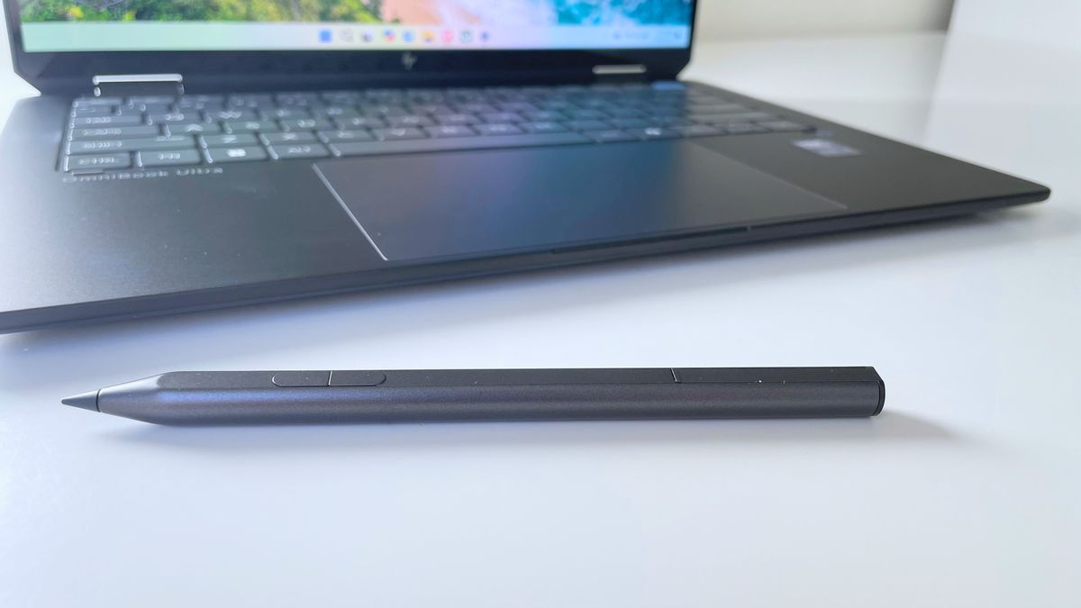 Close up of a digital pen on a white surface with a laptop trackpad and keyboard behind it.