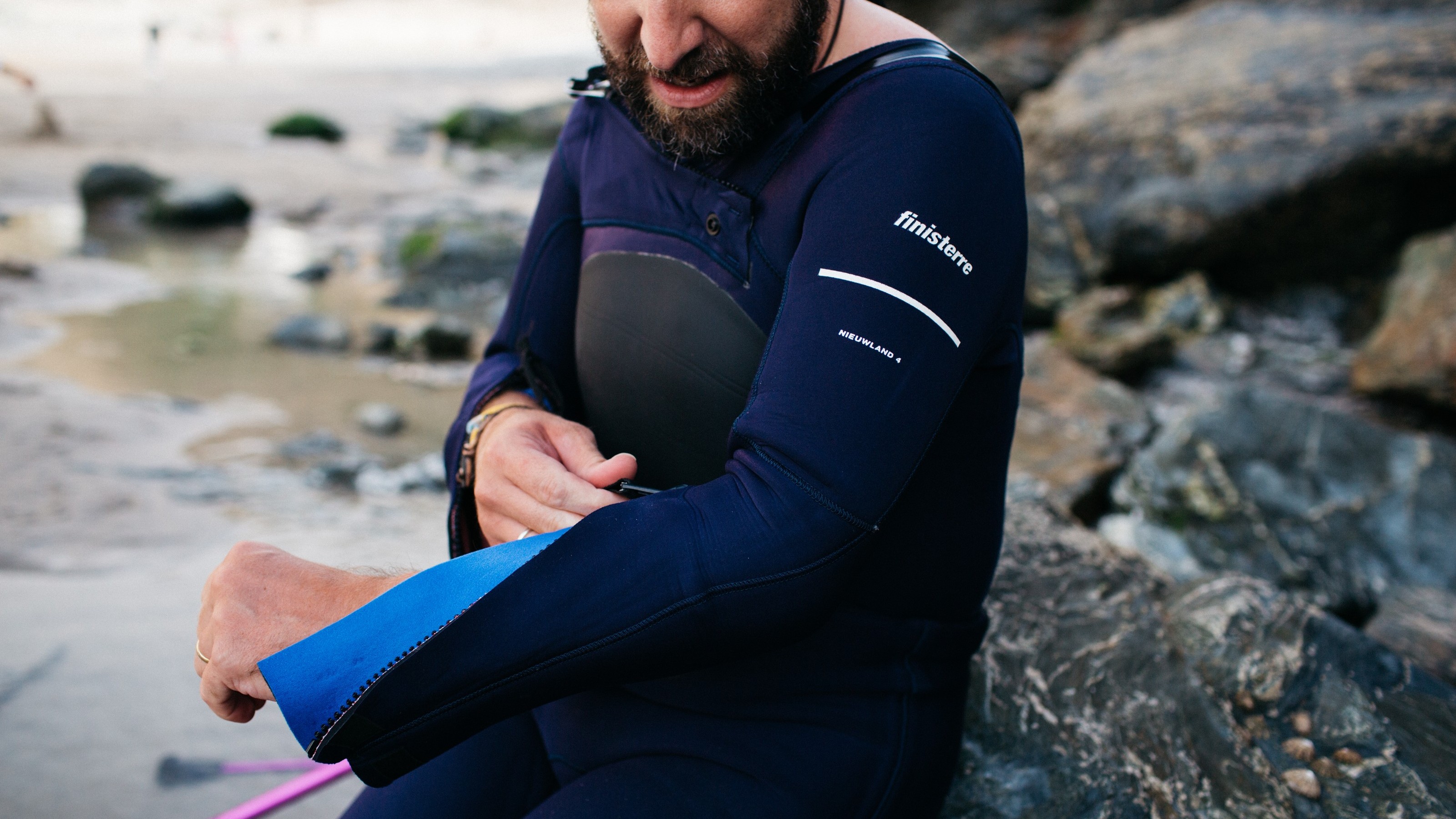 A man unzipping the sleeve of an adaptive Yulex wetsuit with Finisterre logo