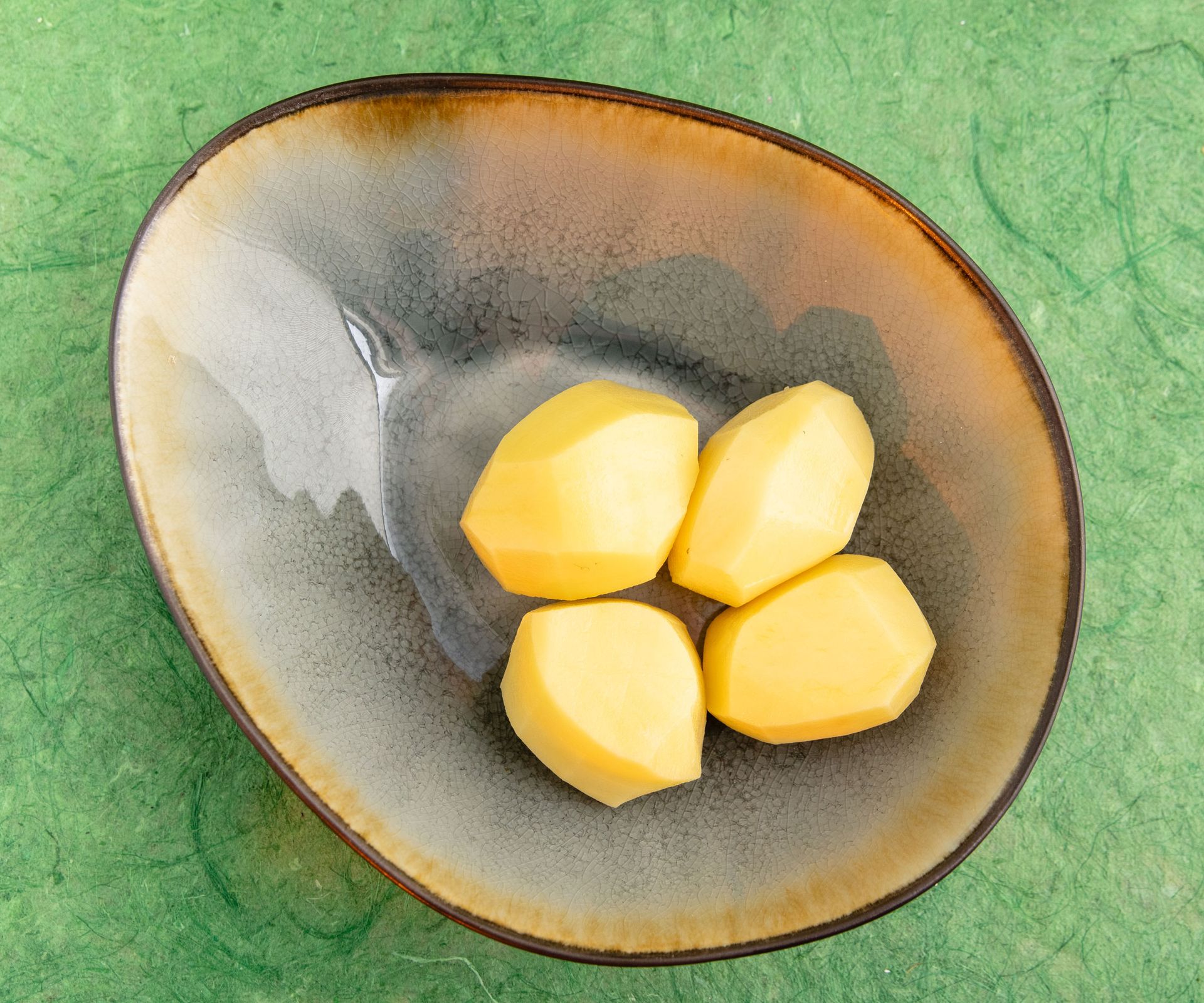 boiled potatoes in glazed ceramic dish on green table