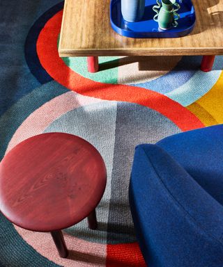 overhead detail of an abstract rug pattern in vibrant colours, with a red side table and blue armchair