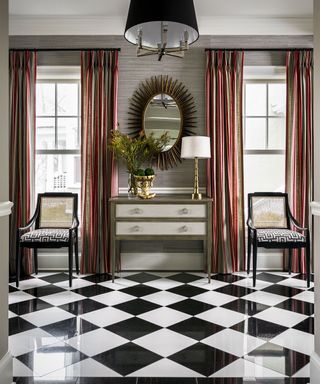 A foyer with black and white checkered floor, and Art Deco-style sunburst mirror and chairs