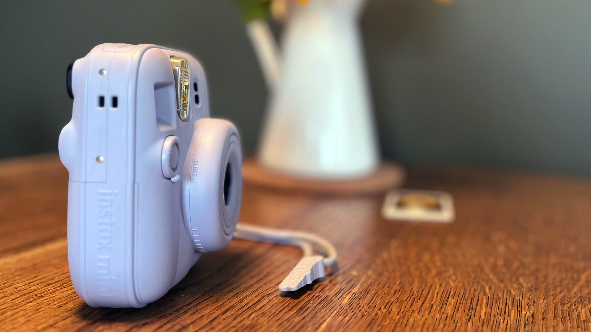 A side profile of the Forst Blue Instax Mini 13 next to a vase of sunflowers